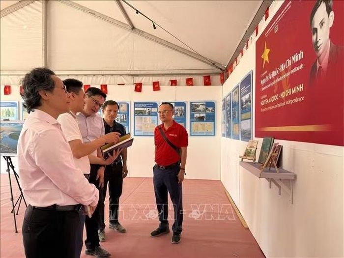 Đại diện Báo Nhân Dân giới thiệu nội dung trưng bày về Chủ tịch Hồ Chí Minh và hành trình đấu tranh giành độc lập của Việt Nam cho Đại sứ Lào tại Pháp Kalamoungkhoune Souphanouvong (đứng giữa). Ảnh: Hữu Chiến/PV TTXVN tại Pháp