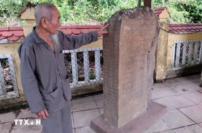 Ông Trà Tấn Tôn, 88 tuổi, Tộc trưởng của cộng đồng người Chăm (thôn Bình An, xã Đồng Dương, thành phố Đà Nẵng), giới thiệu về tấm bia đá có khắc chữ Phạn cổ chứa đựng thông tin về quá trình hình thành Phật viện Đồng Dương vào năm 875. (Ảnh: Đỗ Trưởng/TTXVN)