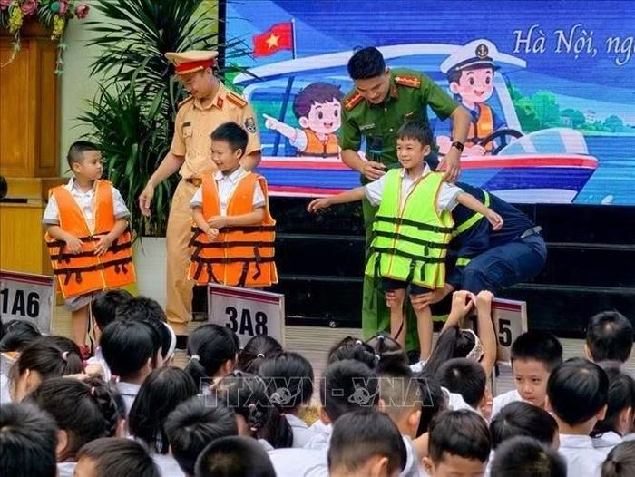 Đại úy Nguyễn Nam Ngọc, báo cáo viên Đội Cảnh sát phòng cháy, chữa cháy và cứu nạn, cứu hộ trên sông, cùng cán bộ Đội Cảnh sát đường thủy số 2, Phòng Cảnh sát giao thông, Công an thành phố Hà Nội hướng dẫn học sinh mặc áo phao đúng cách và phòng, chống đuối nước. Ảnh: Trung Nguyên/TTXVN