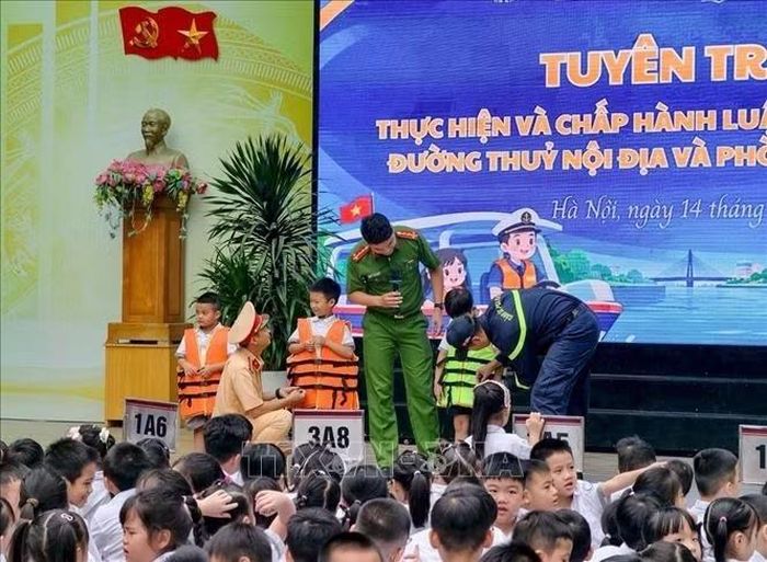 Đại úy Nguyễn Nam Ngọc, báo cáo viên Đội Cảnh sát phòng cháy, chữa cháy và cứu nạn, cứu hộ trên sông, cùng cán bộ Đội Cảnh sát đường thủy số 2, Phòng Cảnh sát giao thông, Công an thành phố Hà Nội hướng dẫn học sinh mặc áo phao đúng cách và phòng, chống đuối nước. Ảnh: Trung Nguyên/TTXVN