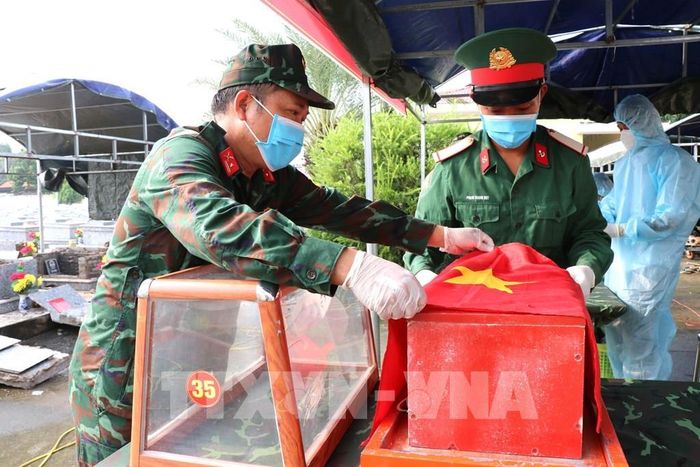 Các chiến sĩ phủ cờ Tổ quốc lên hài cốt liệt sĩ sau khi hoàn thành việc lấy mẫu phục vụ giám định ADN, xác định danh tính. Ảnh: Thanh Hòa - TTXVN
