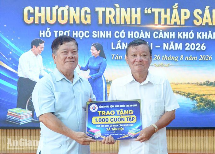 Chủ tịch Hội Bảo trợ bệnh nhân nghèo tỉnh Trương Thắng Trận (bên trái) trao bảng tượng trưng hỗ trợ tập cho học sinh có hoàn cảnh khó khăn ở xã Tân Hội.