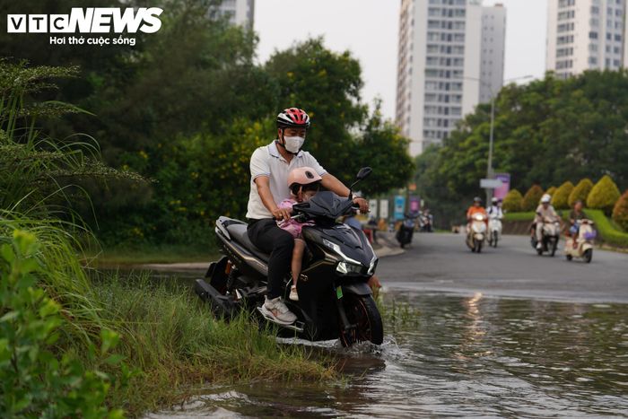 Nước ngập trên đường khiến nhiều phương tiện di chuyển khó khăn. Một số phụ huynh phải đưa xe lên lề đường để tìm cách vượt qua khu vực ngập, đưa con đến trường đúng giờ.