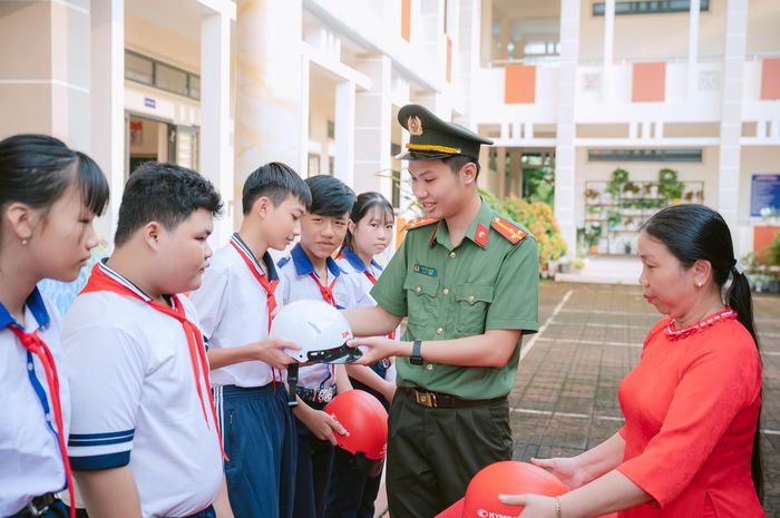 Cán bộ Phòng Công tác chính trị, Công an tỉnh Cà Mau trao tặng mũ bảo hiểm cho các em học sinh (Ảnh: H.Đ).