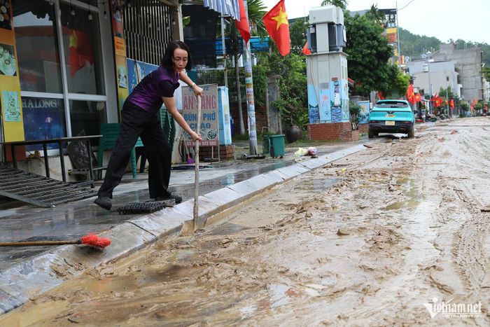 Bà Lê Thị Quyên chủ động dọn dẹp bùn nhão trước cửa nhà. Ảnh: Phạm Công