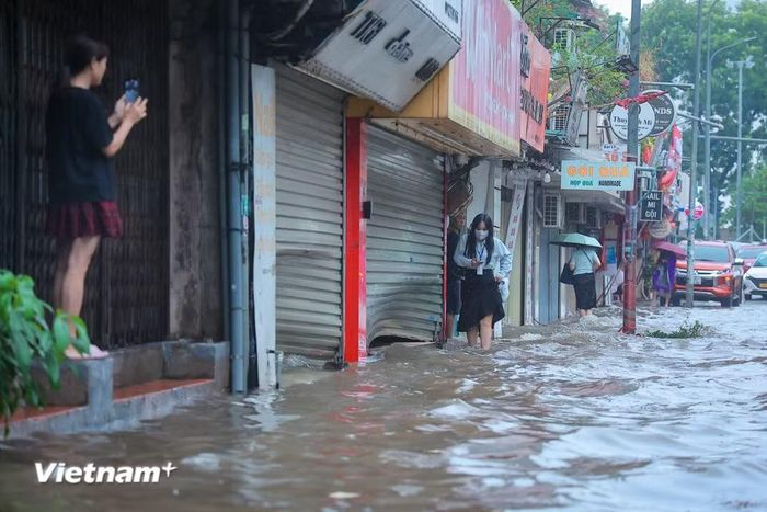 Người dân men theo vỉa hè di chuyển để tránh đoạn ngập nước sâu. (Ảnh: Hoài Nam/Vietnam+)