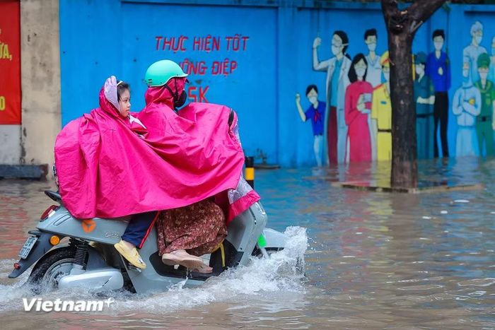 Người dân chật vật đưa con đi học trong cảnh ướt sũng, trước khi tiếp tục vật lộn trên đường đến công sở. (Ảnh: Hoài Nam/Vietnam+)