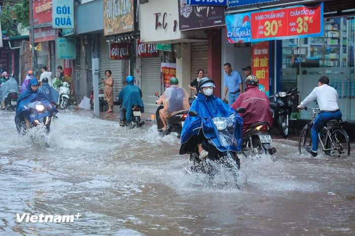 Người dân men theo vỉa hè di chuyển để tránh đoạn ngập nước sâu. (Ảnh: Hoài Nam/Vietnam+)