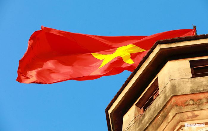 Lá cờ đỏ sao vàng tung bay trên đỉnh Cột cờ trong nền trời thu, tạo nên khoảnh khắc giao hòa giữa vẻ đẹp thơ mộng của Hà Nội và niềm tự hào dân tộc.