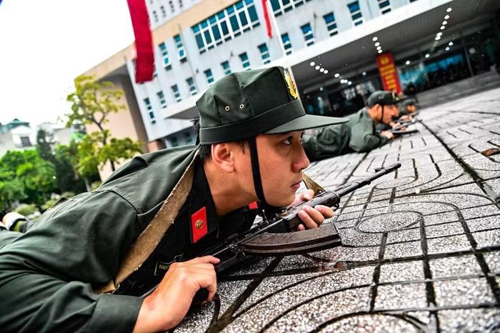 Chiến sĩ mang súng tiểu liên AK thực hiện động tác trườn chiến đấu sát mặt sân ướt đẫm. Đây là kỹ thuật bắt buộc khi cần tiến gần sát đối tượng qua khu vực trống trải, đòi hỏi hạ thật thấp cơ thể và di chuyển hết sức nhẹ nhàng, thận trọng.