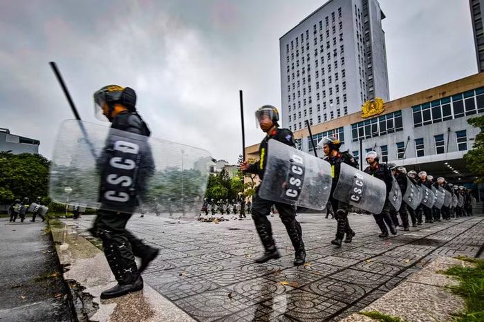 Nước mưa đọng kín bề mặt lớp mica trong suốt. Đằng sau lá chắn ướt sũng là sự điềm tĩnh tuân thủ tuyệt đối kỷ luật. Họ không còn là những cá nhân đơn lẻ ở các phường, xã, mà là mắt xích không thể tách rời của một cỗ máy chiến đấu.