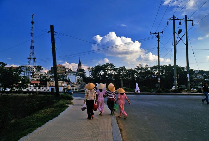 Người dân dạo bộ bên bờ hồ Xuân Hương, phía xa là tháp chuông nhà thờ Con Gà. Con đường chạy quanh hồ uốn theo địa hình, nối khu vực trung tâm với những khoảng xanh và các công trình nghỉ dưỡng, công cộng. Nhờ sự xuất hiện của quảng trường Lâm Viên (nay thuộc phường Xuân Hương - Đà Lạt) năm 2016, khu vực quanh hồ Xuân Hương trở nên nhộn nhịp vào mỗi buổi tối.