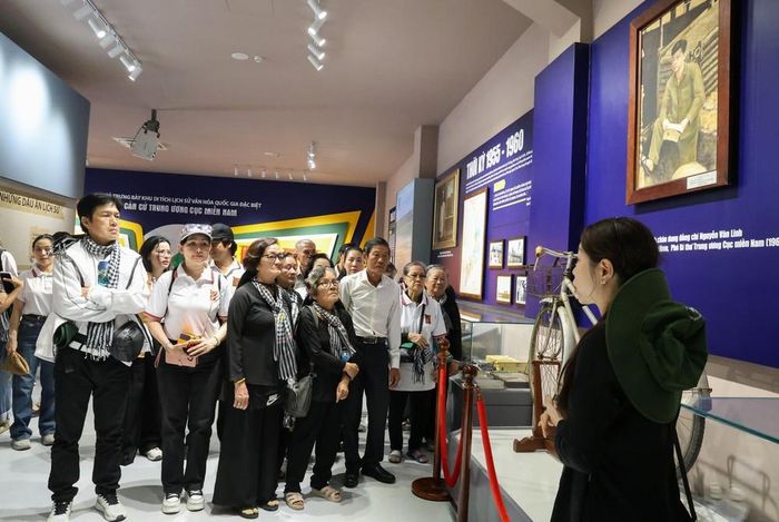 Các nghệ sĩ nghe hướng dẫn viên giới thiệu về những kỷ vật thời kháng chiến được trưng bày tại nhà trưng bày của Khu di tích quốc gia đặc biệt Căn cứ Trung ương Cục miền Nam. Ảnh: Giang Phương - TTXVN