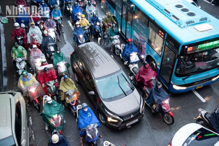Cơn mưa lớn khiến người và phương tiện trên đường phố Hà Nội di chuyển vội vã hơn. Người đi xe máy tìm cách mặc áo mưa, che chắn hành lý, trong khi ô-tô nối dài trên những tuyến đường chính.