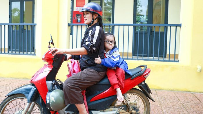 Mẹ em tên là Lê Thị Thi. Mỗi ngày, mẹ đưa em đến trường trên chiếc xe máy quen thuộc. Bận rộn với việc buôn bán ở chợ, mẹ vẫn luôn canh từng giờ để đưa đón em đúng giờ.