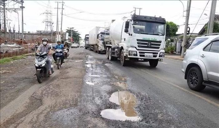 Người đi xe máy phải di chuyển sát mép đường để tránh các vị trí hư hỏng trên đường Nguyễn Huệ, trong khi nhiều xe tải trọng lớn lưu thông qua tuyến.
