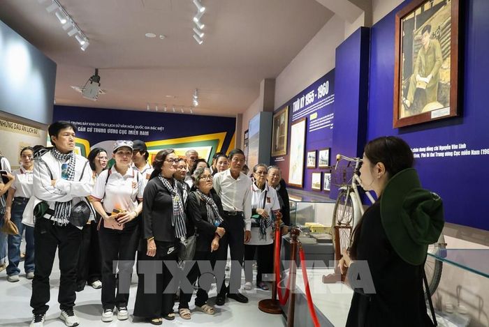 Các nghệ sĩ nghe hướng dẫn viên giới thiệu về những kỷ vật thời kháng chiến được trưng bày tại nhà trưng bày của Khu di tích quốc gia đặc biệt Căn cứ Trung ương Cục miền Nam. Ảnh: Giang Phương - TTXVN