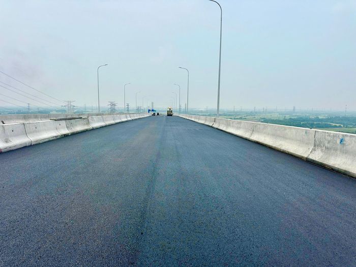 Máy móc đi trước, công nhân theo sau để san gạt, căn chỉnh hoàn thành mặt cầu thảm mịn...