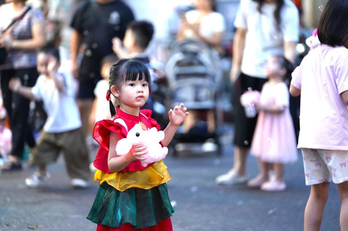  Hình ảnh những em bé được bố mẹ đưa đi mua đồ chơi. Có em chăm chú nhìn những chiếc đèn lồng đủ hình dáng, có em đứng trước cửa hàng rất lâu để chọn một chiếc đầu lân yêu thích. Nhiều phụ huynh thậm chí phải bế hoặc cõng con lên vai để các em có thể nhìn rõ những món đồ chơi được treo cao. 