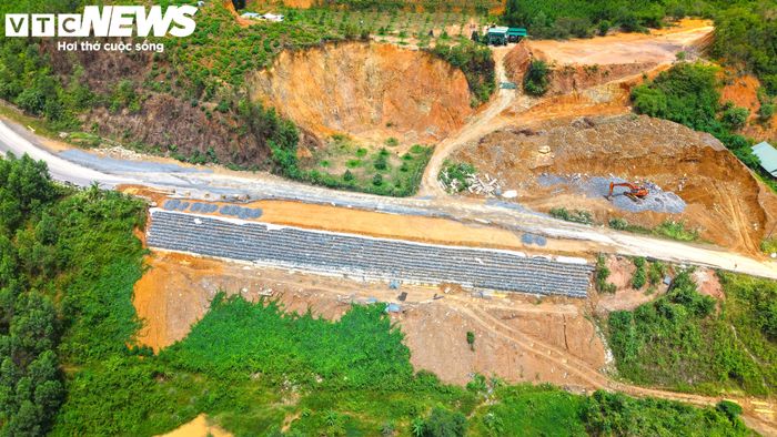 Một đoạn taluy âm trên đèo Khánh Lê đã được gia cố bằng đá, nền đường san phẳng. Ở khu vực lân cận, máy xúc tiếp tục san gạt, rải đá tại taluy dương để chuẩn bị cho các hạng mục gia cố tiếp theo.
