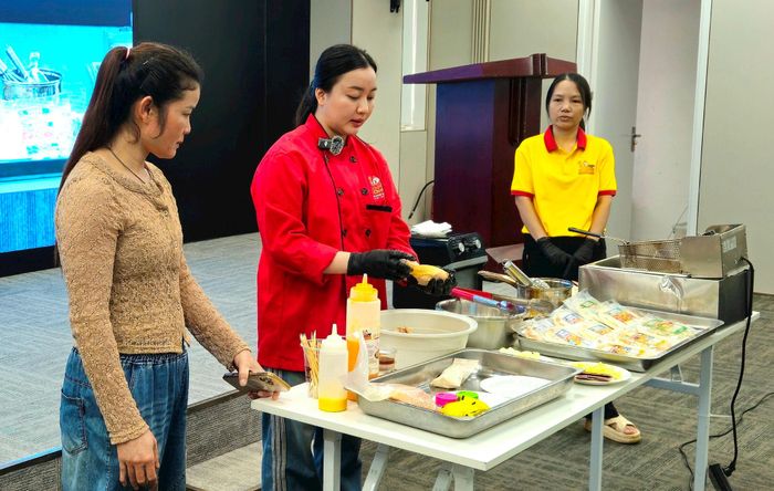 Các chủ cơ sở kinh doanh được chuyên gia hướng dẫn chế biến đồ ăn là gà rán. Ảnh: Ánh Dương