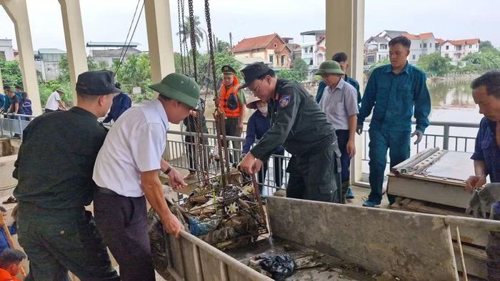 Cảnh sát cơ động phối hợp công nhân thủy lợi dùng ròng rọc tời lồng thép chứa đầy phế thải từ lòng kênh lên máng xe gom.