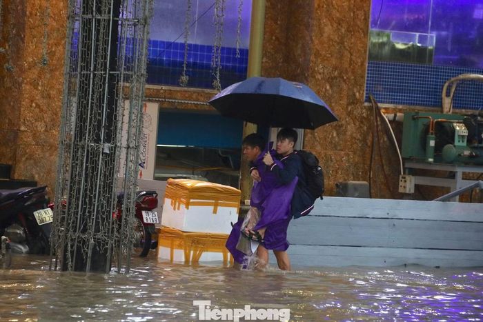 Phụ huynh cõng con đến trường trong cảnh tuyến phố chìm trong biển nước sau mưa lớn.
