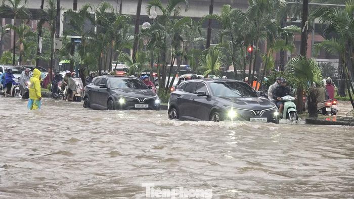 Hàng dài phương tiện nối đuôi di chuyển chậm qua đoạn đường ngập sâu. Nhiều người dò dẫm để tránh những vị trí có thể gây nguy hiểm.