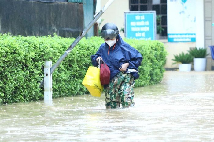 Người nhà bệnh nhân lội qua dòng nước ngập sâu trong khuôn viên Trung tâm Y tế Hoàng Mai.