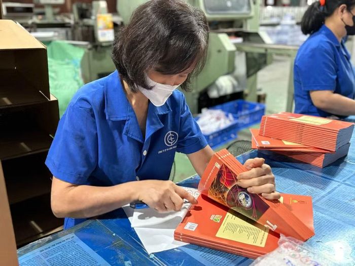 Công nhân thực hiện công đoạn dán tem cho sách giáo khoa. (Ảnh: Phạm Mai/Vietnam+)