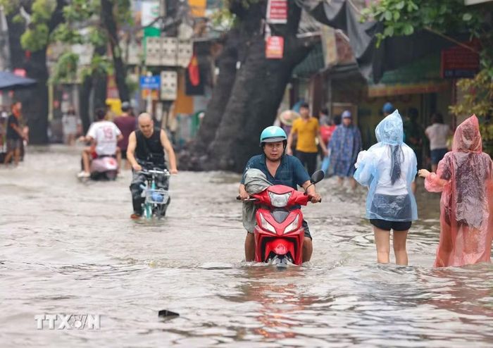 Nhiều xe máy điện vẫn di chuyển qua đường Tây Mỗ đang bị ngập. (Ảnh: Thanh Tùng/TTXVN)