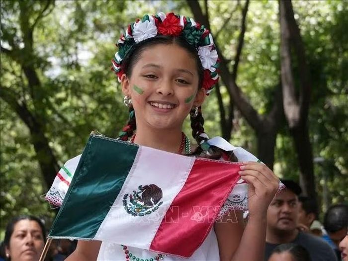 Bé gái cầm quốc kỳ Mexico chào mừng đoàn diễu binh. Ảnh: Phi Hùng/PV TTXVN tại Mexico
