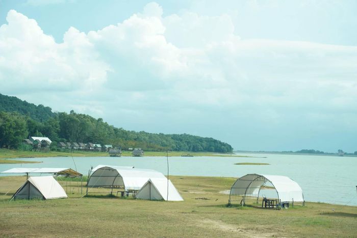 Một điểm cắm trại ven hồ được chuẩn bị sẵn lều, chăn gối và khu vực ăn uống cho khách.