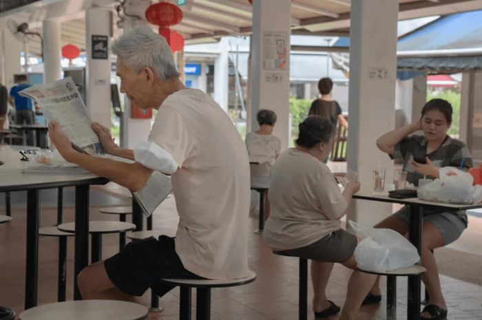 Một người đàn ông đang đọc báo tại chợ và trung tâm ẩm thực Pek Kio ở Singapore. Ảnh: Amrita Chandradas/The Washington Post/Getty Images