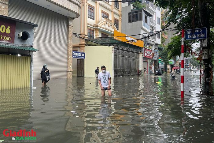 Tại khu vực phố Thiên Hiền và các tuyến đường lân cận, khung cảnh buổi sáng đầu tuần trở nên vô cùng nhốn nháo và khó khăn. Nước ngập sâu khiến việc đi lại của người dân bị đảo lộn hoàn toàn: Nhiều người dân phải xắn cao quần, tháo giày dép, lội bì bõm qua dòng nước ngập để tìm cách di chuyển ra đường lớn.