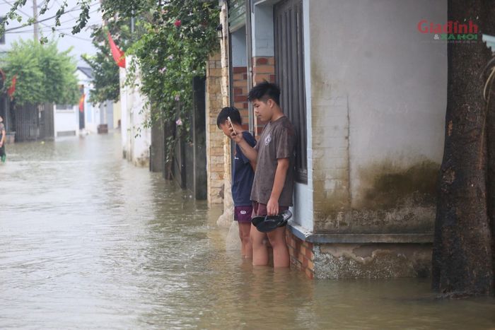 Các em nhỏ lội nước, nép mình trước hiên nhà để tránh mưa. 