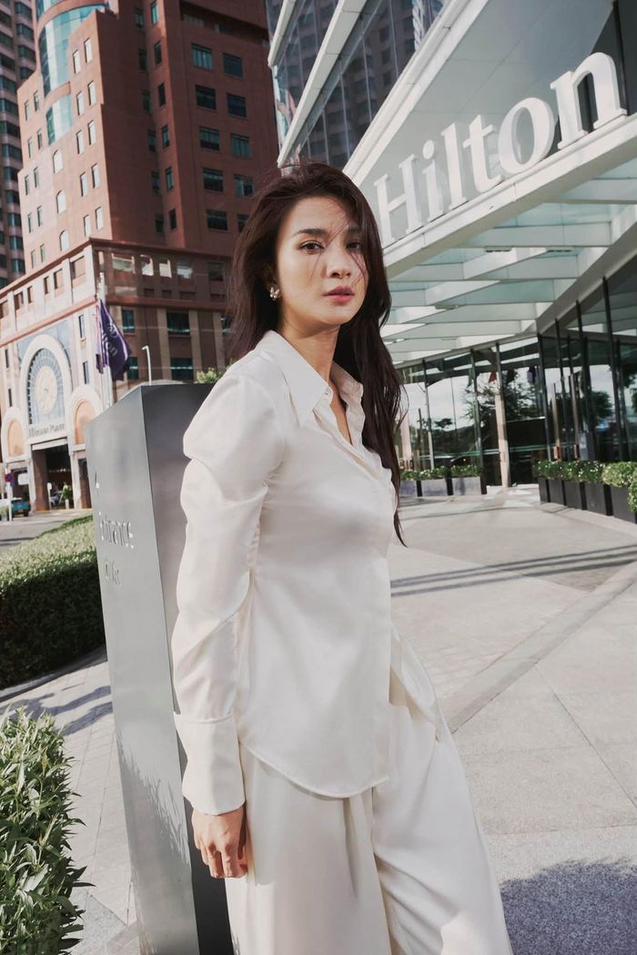 Kim Tuyến diện sơ mi trắng chiết nhẹ, phối cùng quần ống rộng. Thay vì chọn áo có cấu trúc cứng như sơ mi công sở thông thường, cô sử dụng thiết kế mềm, bề mặt có độ bóng vừa phải. Phần cổ mở tự nhiên giúp tổng thể bớt nghiêm nghị, trong khi đường may ôm nhẹ ở thân áo tạo sự gọn gàng.