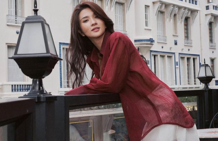 Ở cách phối thứ hai, Kim Tuyến chuyển sang gam đỏ rượu. Chiếc sơ mi dáng rộng, chất liệu mỏng nhẹ được mặc ngoài lớp áo đồng màu, đi cùng chân váy voan trắng xuyên thấu dáng dài.