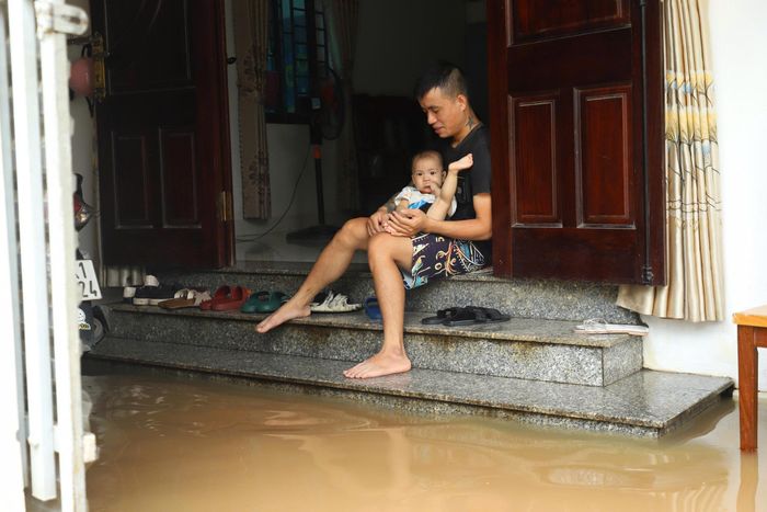 Anh Lê Viết Hưởng cùng con nhỏ trong căn nhà bị nước lũ tràn vào sau nhiều ngày mưa lớn. Ảnh: TIẾN CƯỜNG
