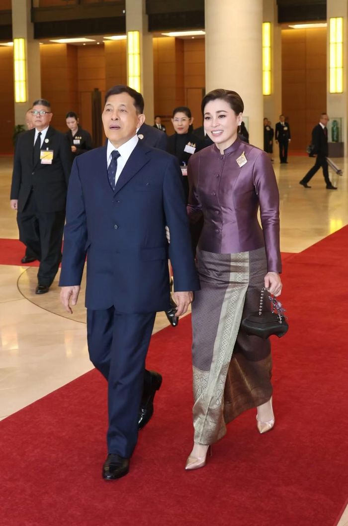Hoàng hậu Suthida tiếp tục mang theo túi Yan Lipao, đi giày cao gót màu nude và ghim cài hình hoa. Ngực trái của bà cài chiếc huy hiệu hình vuông, viền khung chữ nhật. Đây là huy hiệu kỷ niệm lễ đăng cơ của Nhà vua Maha Vajiralongkorn và Hoàng hậu Suthida ngày 1/5/2019.