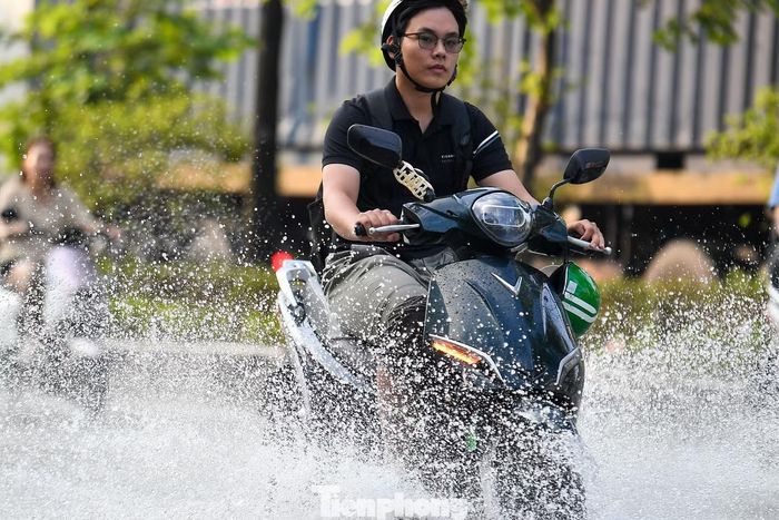 Một người đi xe máy vượt qua đoạn ngập, nước bắn tung tóe sang hai bên.