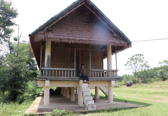 Ông Phạm Văn Nguyên thổi đàn Ra ngói bên nhà sàn truyền thống của đồng bào Hre.