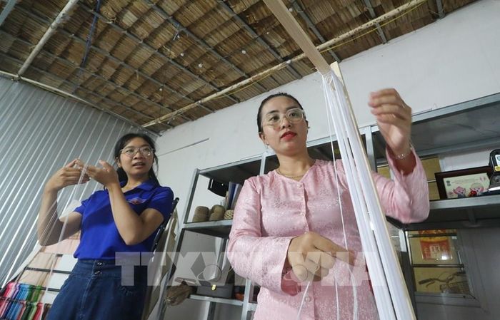 Chị Huỳnh Ngọc Như (bên phải) chia sẻ các công đoạn tạo thành sản phẩm từ lụa sen cho các bạn đoàn viên, thanh niên tham quan. Ảnh: Hồng Thái - TTXVN