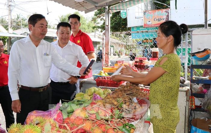 Lãnh đạo UBND xã Song Lộc tuyên truyền, hướng dẫn tiểu thương sử dụng phương thức thanh toán không dùng tiền mặt. Ảnh: Thanh Hòa - TTXVN