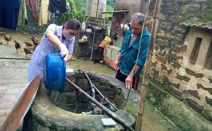 Lực lượng y tế xã Ngọc Liên khử trùng giếng nước sinh hoạt cho các hộ dân bị ngập lụt.