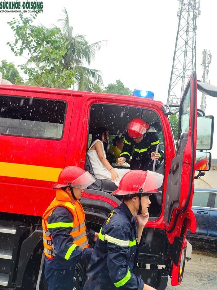 Cán bộ, chiến sĩ Cảnh sát phòng cháy, chữa cháy và Cứu nạn cứu hộ hỗ trợ chị N.T.A. di chuyển qua khu vực ngập sâu, đưa lên xe cứu hộ để đến bệnh viện giữa lúc mưa lớn. Ảnh: C.M