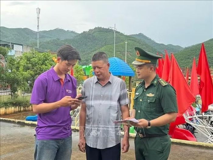 Cán bộ Đồn Biên phòng Cửa khẩu Hoành Mô và nhân viên ngân hàng hướng dẫn người dân thực hiện các thao tác dịch vụ công và thanh toán qua mã QR trên điện thoại thông minh.
