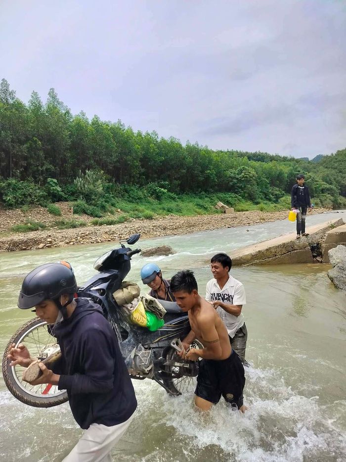 Người dân hỗ trợ đưa xe máy qua đoạn tràn có dòng nước chảy xiết trên đường vào thôn Cát Trỉa. Ảnh: CTV