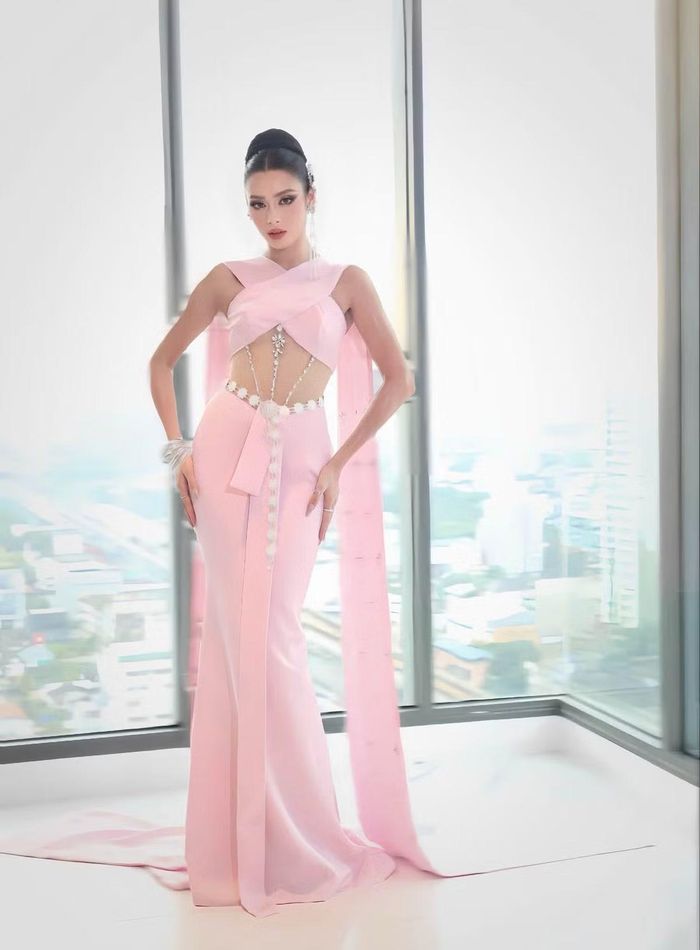 Emoura Phạm thử nghiệm thiết kế màu hồng với những khoảng cut-out ở eo, kết hợp chi tiết đính kết chạy dọc thân. Kiểu tóc búi cao và cách tạo dáng nhấn vào lợi thế hình thể của người đẹp.