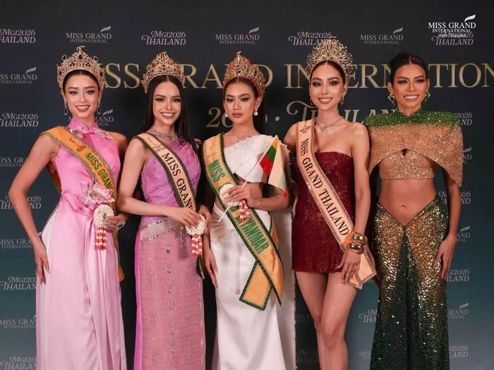 Emoura Phạm xuất hiện bên các thí sinh quốc tế trong một hoạt động của cuộc thi. Người đẹp Việt diện trang phục tông hồng, kết hợp sash Miss Grand Vietnam 2026 và kiểu tóc búi gọn.